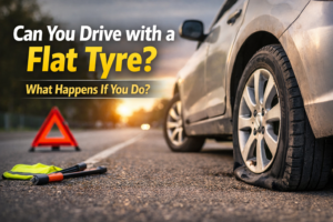 Can you drive with a flat tyre showing damaged car tire on roadside with warning triangle at sunset
